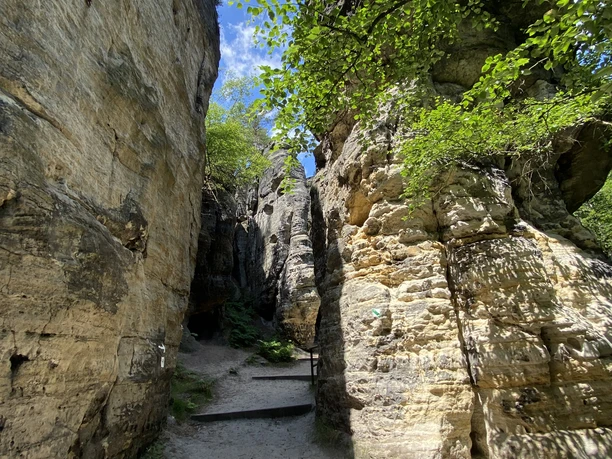 Narrow hiking trail between high rock faces under a blue sky.