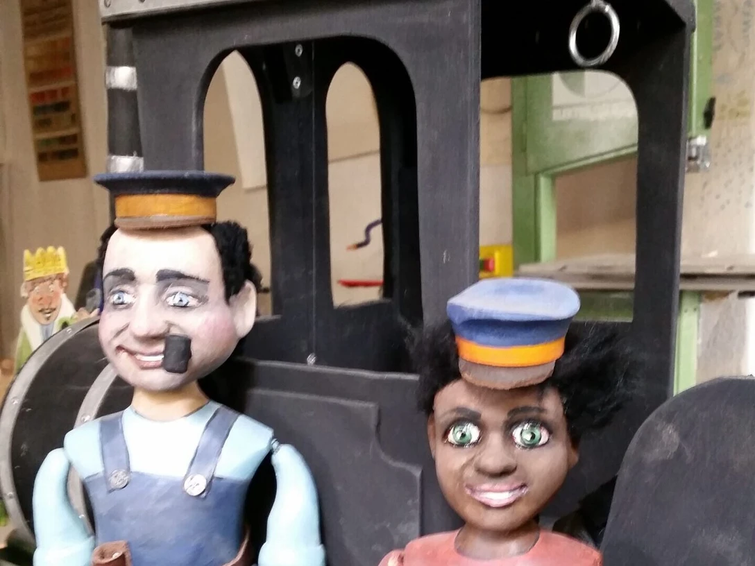Jim Knopf Zwei Holzfiguren von Lokführer Lukas und Jim Knopf vor einer schwarzen Lokomotive.