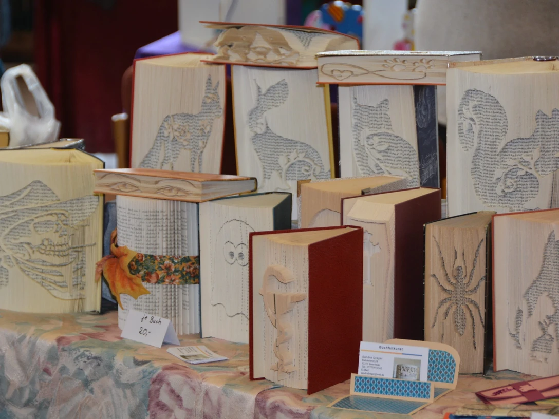 Buchfaltkunst Mehrere gefaltete Bücher mit kunstvollen Motiven wie Tieren, Figuren und Symbolen auf einem Tisch.