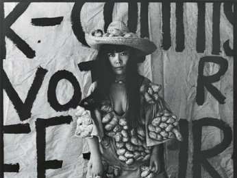 Yayoi Kusama poses in Untitled (Dress) with her phallic sculptures in her New York studio, 1971 Eine Frau posiert in einem Gewand mit knotigen Formen, umgeben von Schuhen und einem Koffer.A woman poses in a robe with knotty shapes, surrounded by shoes and a suitcase.