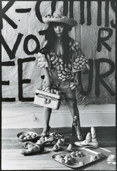 Yayoi Kusama posiert 1971 in ihrem New Yorker Atelier in Untitled (Dress) mit ihren phallischen Skulpturen Eine Frau posiert in einem Gewand mit knotigen Formen, umgeben von Schuhen und einem Koffer.