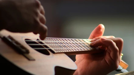 Ukulele Nahaufnahme einer Hand, die eine Ukulele spielt und über die Saiten greift.