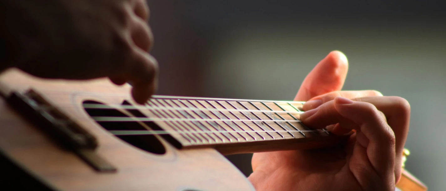 Ukulele Nahaufnahme einer Hand, die eine Ukulele spielt und über die Saiten greift.