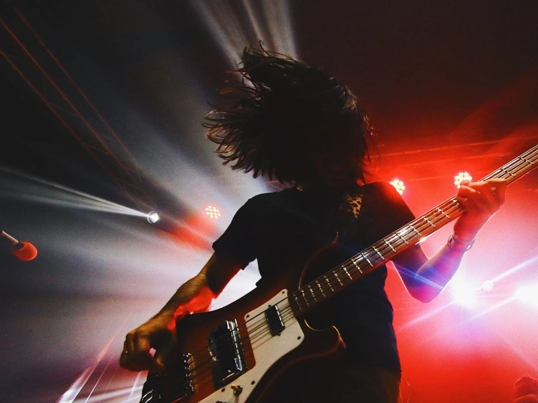 Rockin‘ Between The Years Gitarrist auf einer Bühne mit beleuchtetem Hintergrund in Rot und Weiß, dynamische Konzertszene.