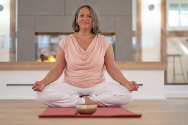 4 - DSC07588.jpg Frau sitzt entspannt im Schneidersitz auf einer Yogamatte vor einem Kamin und meditiert.