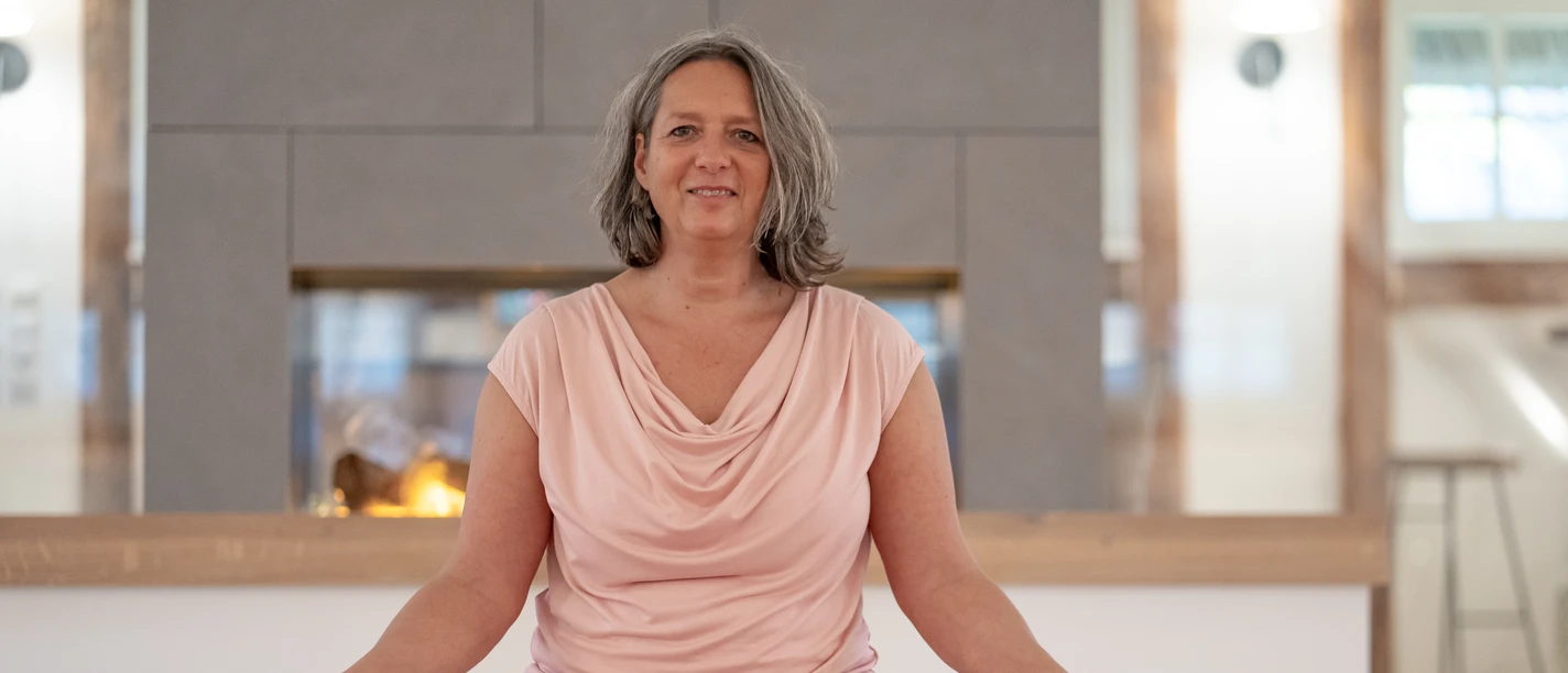 4 - DSC07588.jpg Frau sitzt entspannt im Schneidersitz auf einer Yogamatte vor einem Kamin und meditiert.