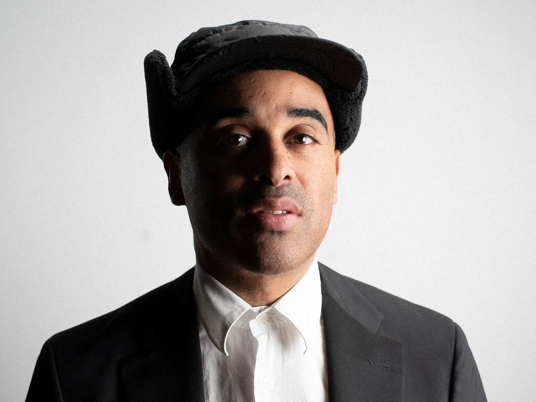 Patrice Eine Person mit dunklem Anzug und weißem Hemd, lächelt leicht. Schwarze Kappe auf dem Kopf.A person in a dark suit and white shirt, smiling slightly. Black cap on his head.