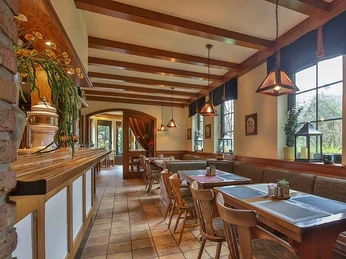 hotel_berghof_galerie_08.jpg Helles Restaurant mit Holzmöbeln, Theke und großen Fenstern mit Blick ins Grüne.