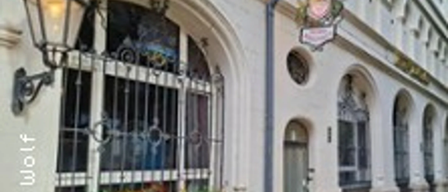 Historische Hausfassade mit Laternen, verziertem Fenster und Laub auf dem Gehweg