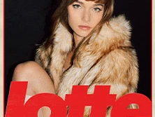 Eine Frau mit Pelzmantel blickt direkt in die Kamera, umgeben von dunklem Hintergrund.