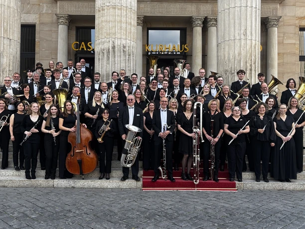 Orchester Ein großes Ensemble von Musikerinnen und Musikern posiert in eleganter schwarzer Kleidung auf den Stufen eines Gebäudes mit Säulen.
