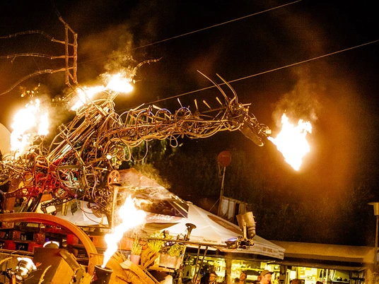 Robodonien Ein feuerspeiender, metallener Drache bei Nacht, umgeben von Kabeln und Schläuchen.A fire-breathing, metal dragon at night, surrounded by cables and hoses.