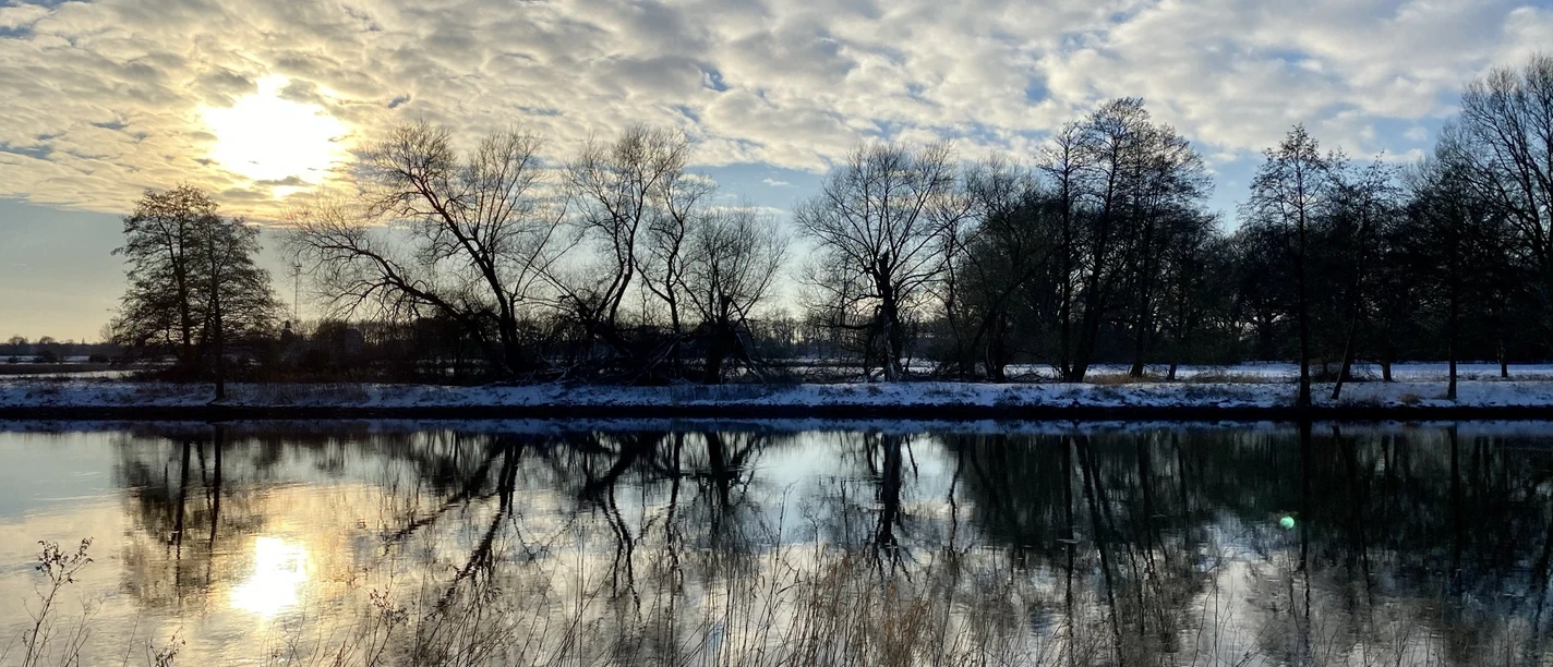 Spaziergang an der Ems - Schnee im Winter ©Naturpark Moor-Veenland (7).jpeg Verschneite Flusslandschaft an der Ems mit winterlicher Sonne und spiegelnden Bäumen im Wasser.