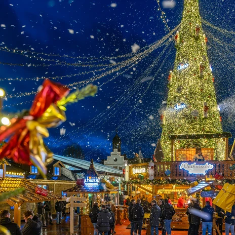 Weihnachtsmarkt Lingen – Marktplatz 2024 ©Lingen Wirtschaft & Tourismus GmbH.jpg Beleuchteter Weihnachtsmarkt in Lingen mit großem Lichterbaum, Buden und Besuchern im Schneefall