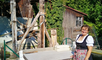 Wasserläufe, Mühlen und Industrie -Die Wasserführung Frau in traditioneller Tracht steht lächelnd vor alter Holz-Mühle mit grünen Pflanzen im Hintergrund.