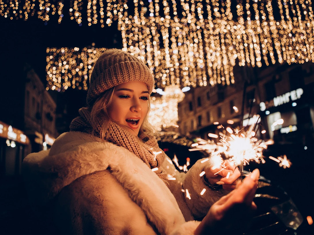 Weihnachtssingen-Bad-Zwischenahn.jpg Frau mit Wollmütze hält Wunderkerze unter festlicher Lichterdekoration beim Weihnachtssingen.