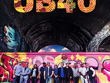 Die Band UB40 steht vor einer bunt bemalten Wand unter einem dunklen Brückenbogen.