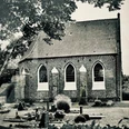 Erlebnistour Kapelle Vreschen-Bokel.jpg Historische Backsteinkapelle mit Spitzbogenfenstern, umgeben von Bäumen und gepflegtem Friedhof in schwarz-weiß