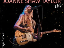 Joanne Shaw Taylor spielt elektrische Gitarre auf einer Bühne vor einem dunklen Hintergrund.