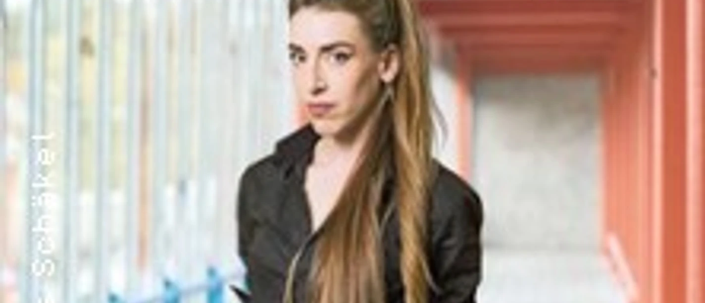 Eine Frau mit langen braunen Haaren steht in einem überdachten, rot-blauen Korridor.
