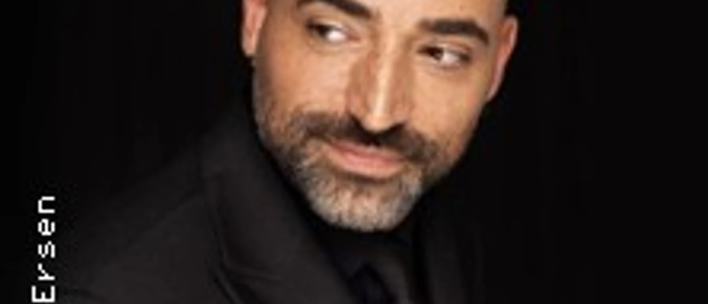 Porträt eines Mannes in dunklem Anzug vor schwarzem Hintergrund, rechts blickend.