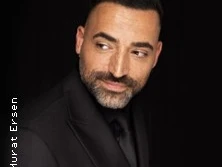 Porträt eines Mannes in dunklem Anzug vor schwarzem Hintergrund, rechts blickend.