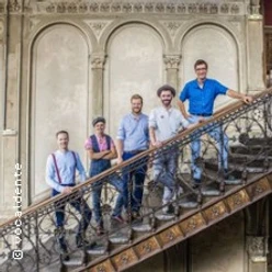 Fünf Personen posieren lächelnd auf einer alten, kunstvoll gestalteten Treppe.