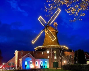 A brightly lit windmill in Pewsum at night, with colorful lighting effects on the building.