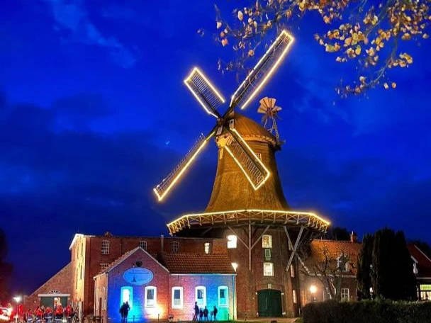 Mühle Pewsum Anleuchtfest Hell erleuchtete Windmühle in Pewsum bei Nacht mit bunten Lichteffekten am Gebäude.