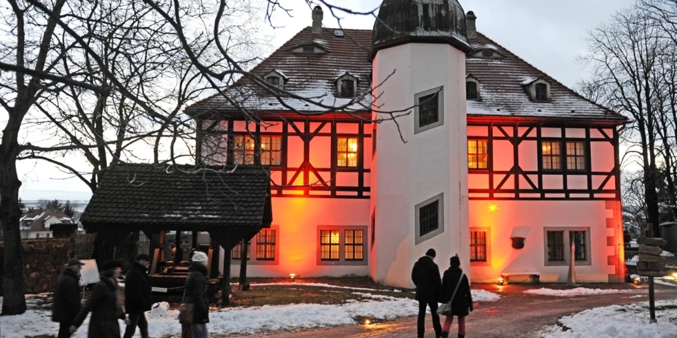 Hoflößnitzer_Weihnacht_Stiftung_Hofloessnitz.jpg Menschen folgen einem verschneiten Weg zu einem rot erleuchteten Fachwerkgebäude