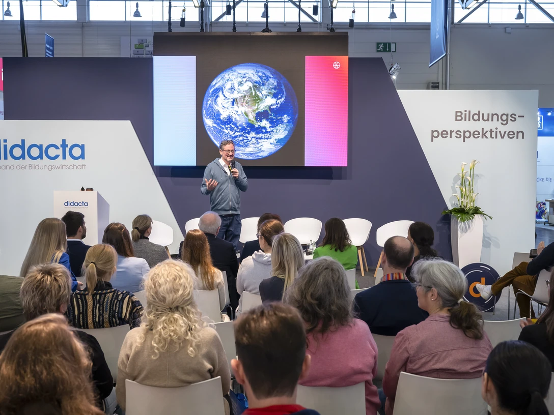 didacta Ein Vortragender steht vor einem Publikum in einem Konferenzraum. Auf der Leinwand ist die Erde zu sehen.A speaker is standing in front of an audience in a conference room. The earth can be seen on the screen.