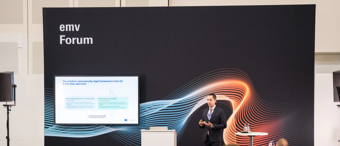 A conference speaker presents content to an audience at a trade fair entitled "emv Forum".