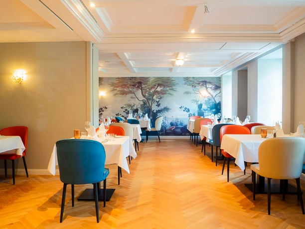 Altenberger Hof Hotel Heller Speiseraum mit bunten Polsterstühlen, gedeckten Tischen und Wandbild mit Landschaft