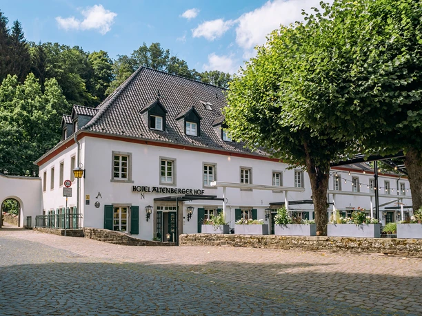 Altenberger Hof Hotel Weißes Hotelgebäude des Altenberger Hofs mit dunklem Dach, grünen Läden und Außenbereich.