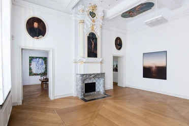 Kunsthaus NRW © Carl Brunn.jpg Museum mit einem Kamin in einem lichtdurchfluteten Raum. Die hohen, weiß gestrichenen Wände sind mit kunstvollen Gemälden dekoriert, darunter ein Porträt und abstrakte Kunstwerke. Holzboden verleiht dem Raum Wärme und Eleganz.