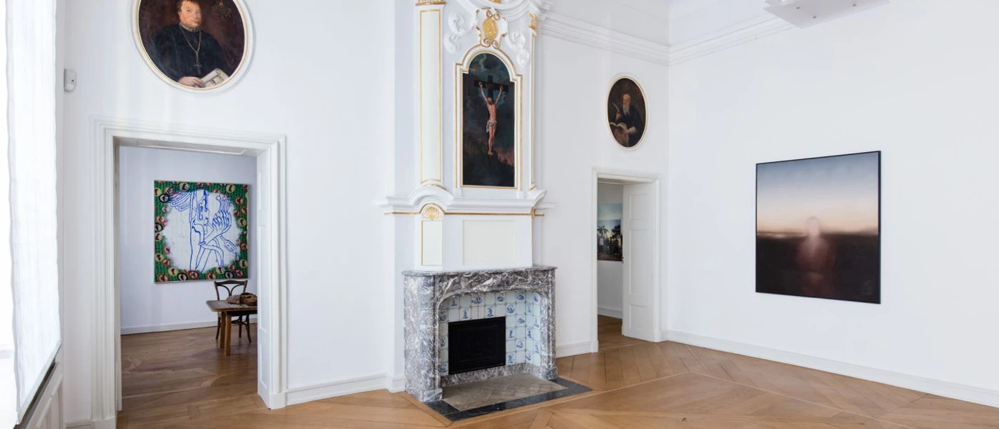 Kunsthaus NRW © Carl Brunn.jpg Museum mit einem Kamin in einem lichtdurchfluteten Raum. Die hohen, weiß gestrichenen Wände sind mit kunstvollen Gemälden dekoriert, darunter ein Porträt und abstrakte Kunstwerke. Holzboden verleiht dem Raum Wärme und Eleganz.