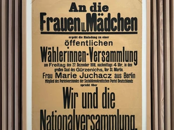 Blick in die Ausstellung "Wegbereiterinnen des Wandels" Plakat im Holzrahmen verkündet Aufruf zur politischen Versammlung der Frauen und Mädchen im Jahr 1918.Poster in a wooden frame announcing the call for a political assembly of women and girls in 1918.