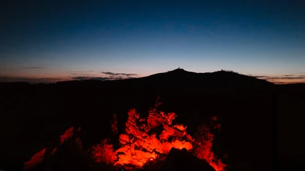 Rot beleuchtete Mauseklippe vor der Silhouette des Brockens in der Abenddämmerung.
