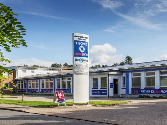 NeuesBild-Fischer-Schuhprofi.jpg Flachbau mit blauer Fassade und großem Firmenschild von Fischer Schuhprofi bei sonnigem Wetter.