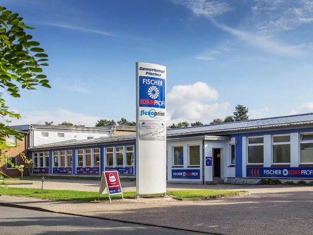 NeuesBild-Fischer-Schuhprofi.jpg Flachbau mit blauer Fassade und großem Firmenschild von Fischer Schuhprofi bei sonnigem Wetter.