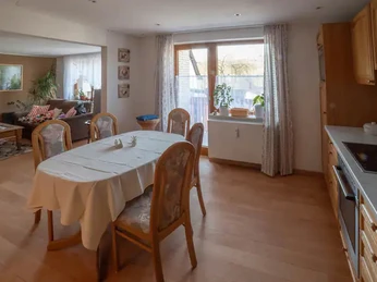 Ferienwohnung am Waldrand Essbereich mit Holztisch, Stühlen und offener Küche, angrenzend an ein Wohnzimmer mit Sofa.