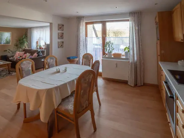 Ferienwohnung am Waldrand Essbereich mit Holztisch, Stühlen und offener Küche, angrenzend an ein Wohnzimmer mit Sofa.
