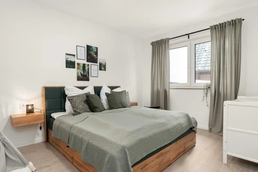 Ferienwohnungen EasyHood Schlafzimmer mit Doppelbett, grüner Bettwäsche, Holzmöbeln und Wandbildern über dem Bett.