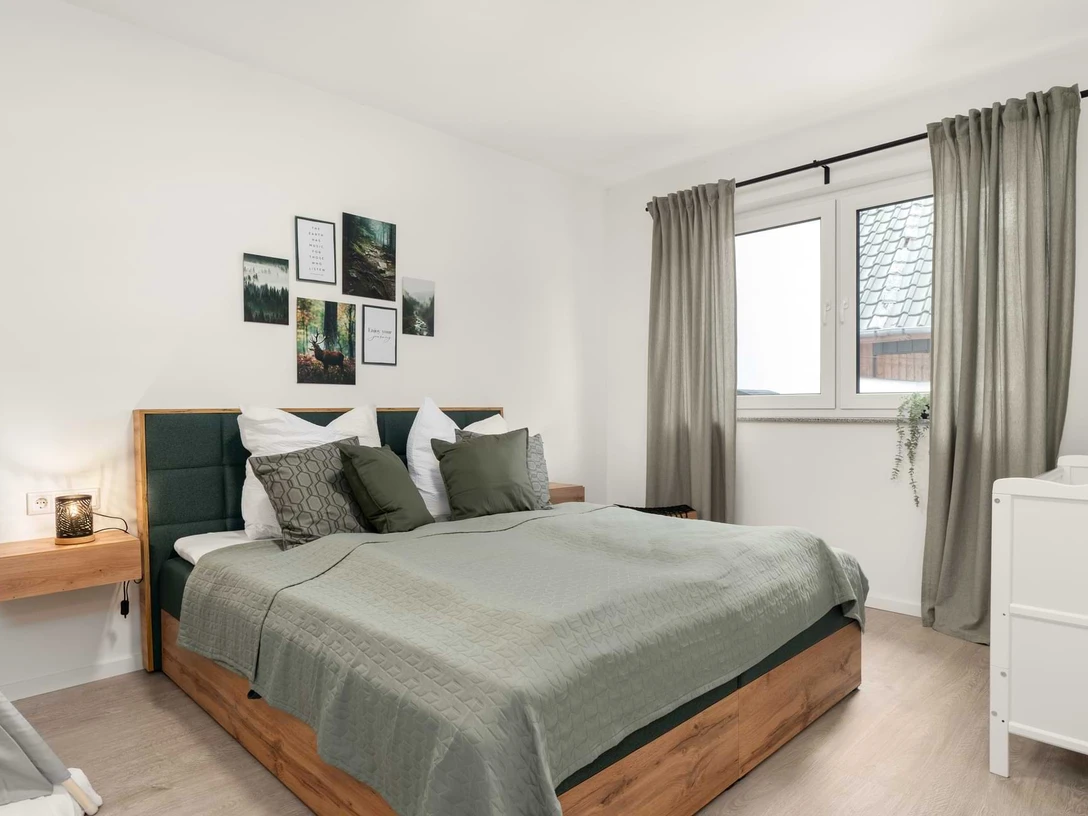 Ferienwohnungen EasyHood Schlafzimmer mit Doppelbett, grüner Bettwäsche, Holzmöbeln und Wandbildern über dem Bett.