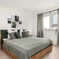 Ferienwohnungen EasyHood Schlafzimmer mit Doppelbett, grüner Bettwäsche, Holzmöbeln und Wandbildern über dem Bett.