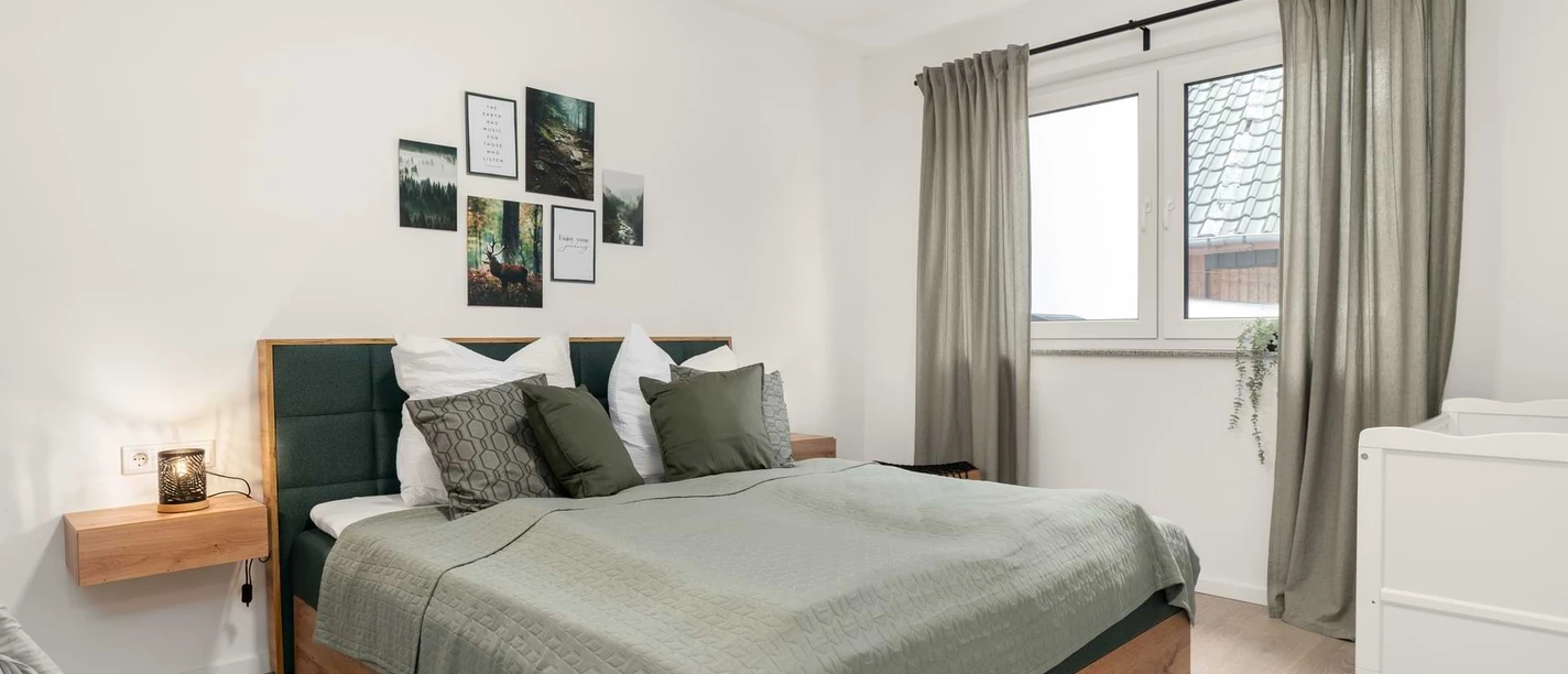 Ferienwohnungen EasyHood Schlafzimmer mit Doppelbett, grüner Bettwäsche, Holzmöbeln und Wandbildern über dem Bett.