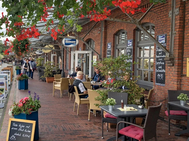 Menschen sitzen vor Backsteinfassaden im Schaufenster Fischereihafen Bremerhaven bei Speisen und Getränken.
