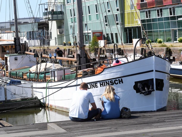 Zwei Personen sitzen am Kai vor dem Segelschiff Line Hinsch im Schaufenster Fischereihafen Bremerhaven.