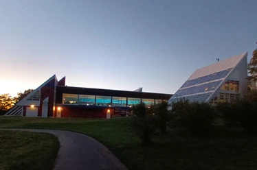 Thermaal pekelbad met verlicht binnenbad tegen een blauwe avondlucht en groene weide.