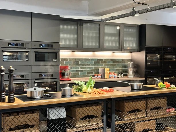IMG_8823.jpg Modern kitchen with black cupboards, cooking islands and fresh vegetables on a wooden counter.